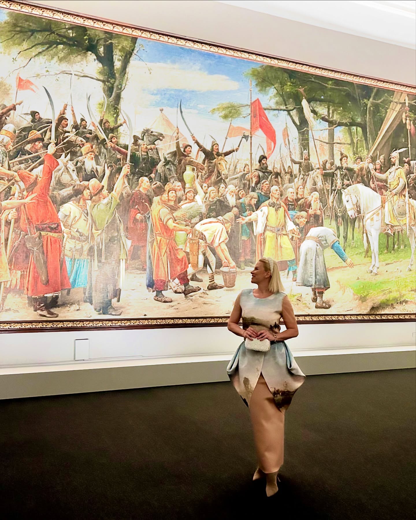 Kovács Erika egy kiállítótérben, nagyméretű festmény előtt