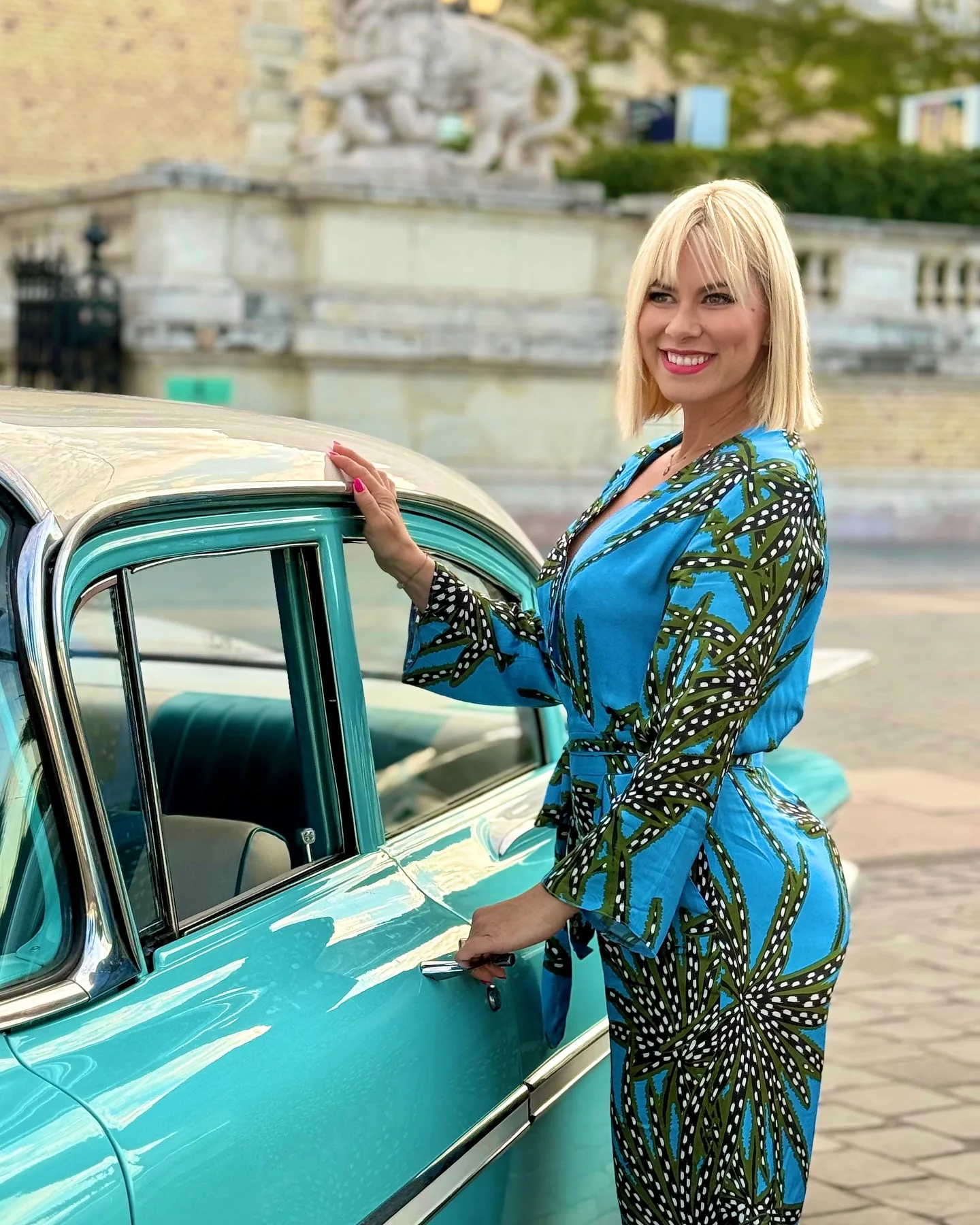 Kovács Erika egy mintás ruhában egy klasszikus autó mellett